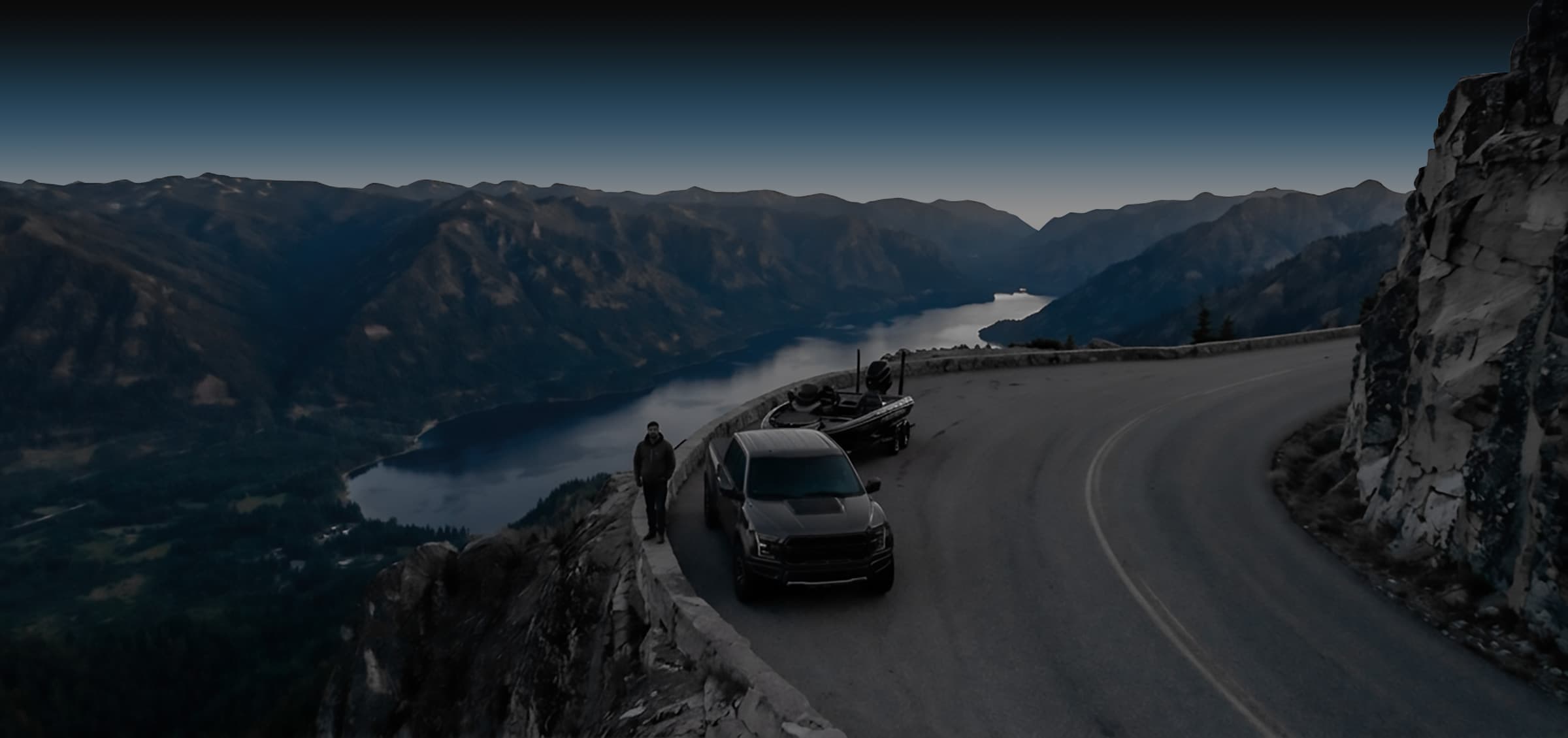 Angler beside his truck and bass boat on a mountain road overlooking a lake at dusk